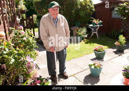 Elderly man with a walking stick in his garden smiling Stock Photo