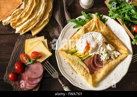 Crepe galette with meat, avocado, soft white cheese and poached egg on white plate Stock Photo