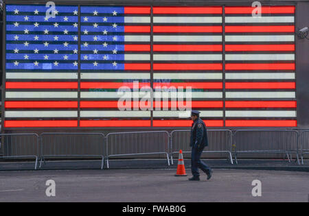 Cop walks in front of a sign of the US flag in Times Square New York Stock Photo