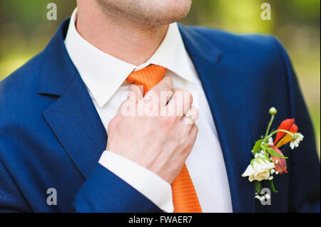 Groom in white shirt and blue suit correcting a orange tie. Ring on his finger. beautiful boutonniere on suit of groom. Man in b Stock Photo