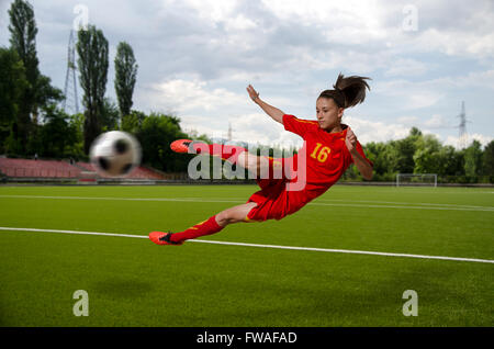 Female football player kicking the ball in the mid-air. Stock Photo