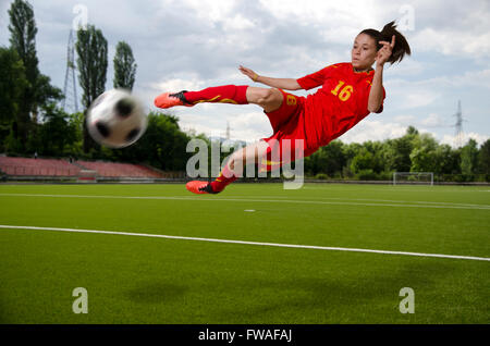 Female football player kicking the ball in the mid-air. Stock Photo