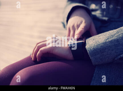 Female using her trendy smart wrist watch. This person is always connected to social media and internet. Modern technology and vintage hipster film toning Stock Photo
