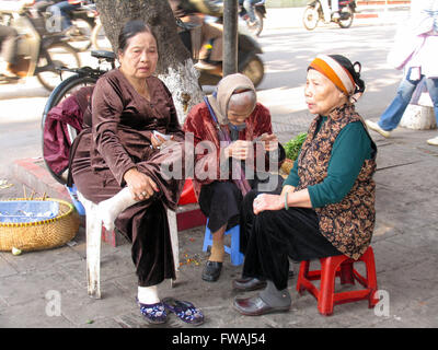 Three elderly Vietnamese women sitting on stools on the sidewalk. Stock Photo