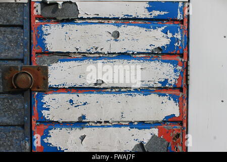 Peeling red, white and blue paint on old metal garage door Stock Photo
