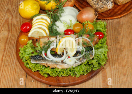 Smoked mackerel fillet with salad, lemon, onions, tomato, garnished with dill on a wooden kitchen board Stock Photo