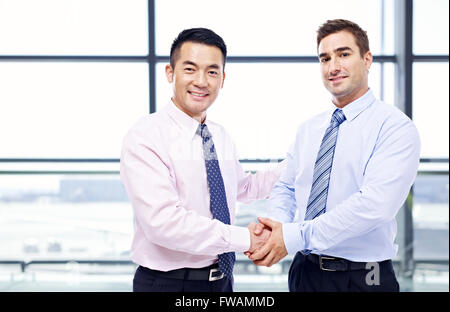 asian and caucasian businessmen shaking hands at airport. Stock Photo