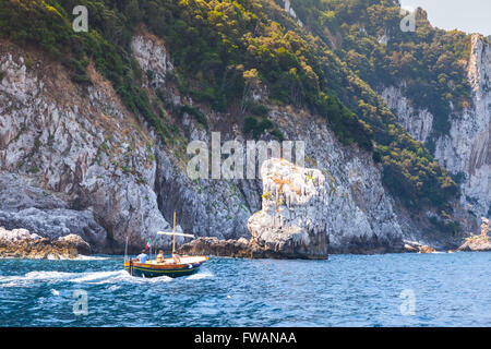 Capri, Italy - August 14, 2015: Small pleasure motorboat with ordinary tourists go near coastal rocks of Capri island, Italy Stock Photo