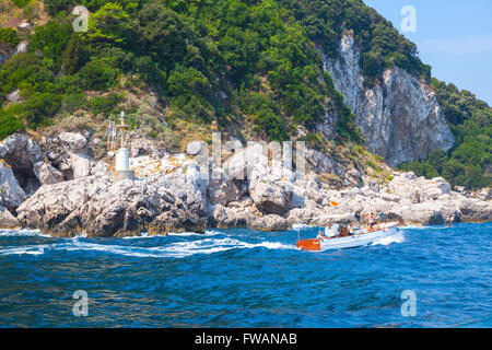 Capri, Italy - August 14, 2015: Small pleasure motorboat with tourists goes near coastal rocks of Capri island, Italy Stock Photo