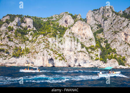 Capri, Italy - August 14, 2015: Small pleasure motorboats with ordinary tourists go near coastal rocks of Capri island, Italy Stock Photo