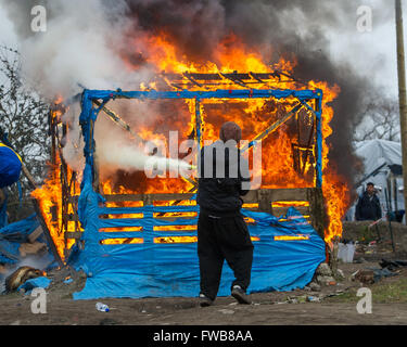 A shack catches fire and French riot police of the Compagnies Républicaines de Sécurité (CRS) use their riot shields to shelter from hailstones during the eviction of refugees and migrants at the Calais Jungle in Northern France.  Featuring: View Where: C Stock Photo