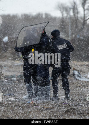 A shack catches fire and French riot police of the Compagnies Républicaines de Sécurité (CRS) use their riot shields to shelter from hailstones during the eviction of refugees and migrants at the Calais Jungle in Northern France.  Featuring: View Where: C Stock Photo