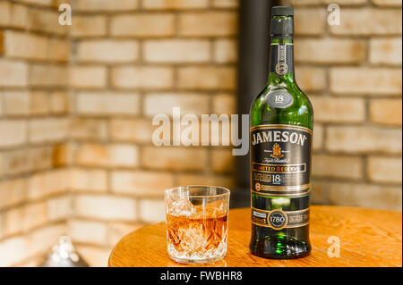 Bottle of 18 year old Jameson triple distilled limited reserve Irish whiskey with a glass of the whiskey with ice cubes on a table with copy space. Stock Photo