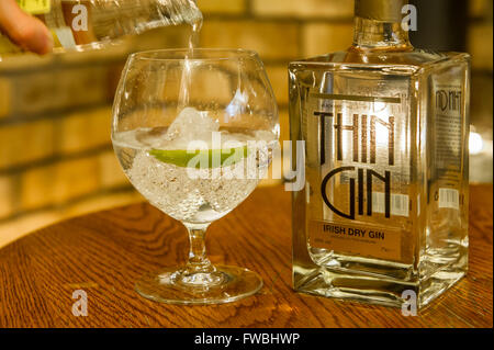 Bottle of Thin Gin with a woman pouring tonic into a glass of gin with ice cubes and  lime. Stock Photo