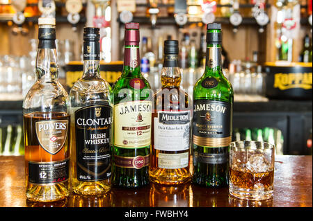 5 bottles of whiskey and a glass of whiskey with ice cubes on a bar counter top in Ireland. Stock Photo