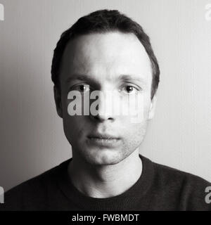 Young serious Caucasian man, close-up square studio portrait over gray wall, black and white photo Stock Photo