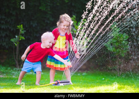 Child playing with garden sprinkler. Preschooler kid running and jumping. Summer outdoor water fun in the backyard. Stock Photo