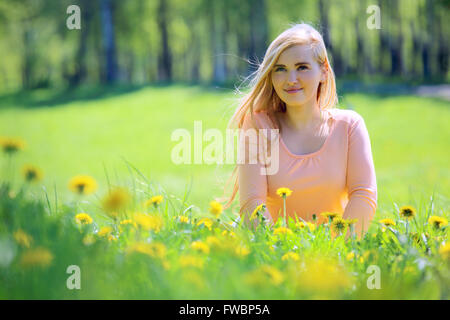 Beautiful young woman laying in spring park with dandelion flowers Stock Photo