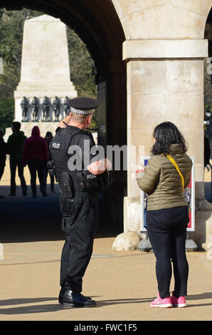 Armed policeman in London with lone female tourist outside of Horse Guards in Whitehall, London, UK. Single police officer with gun, looking away Stock Photo