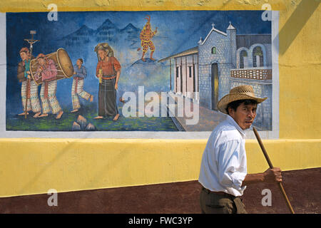 Local man walking in front of a wall panting in San Juan La Laguna, Sololá, Guatemala. Traditional mayan painting art Santiago A Stock Photo