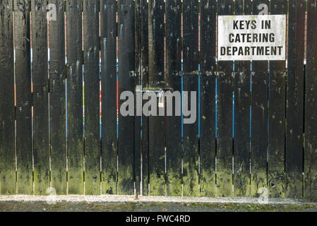 Sign on a locked wooden gate advising people that the keys are available from the catering department. Stock Photo