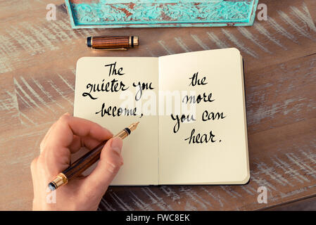 Retro effect and toned image of a woman hand writing on a notebook. Handwritten quote The quieter you become, the more you can hear as inspirational concept image Stock Photo