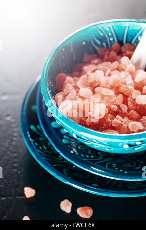 Himalayan Pink Salt Crystals Close Up in a Blue Ceramic Authentic Bowl on a Dark Wooden Surface. Selective Focus. Stock Photo