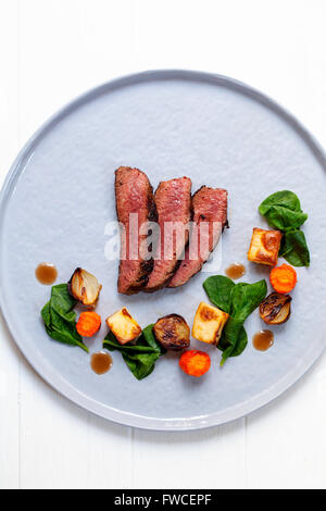 Sliced beef fillet with wilted spinach, potatoes, carrots and shallots Stock Photo