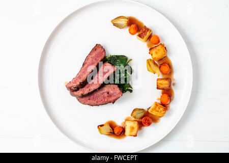 Sliced beef fillet with wilted spinach, potatoes, carrots and shallots Stock Photo