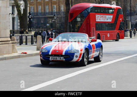 An open top Jaguar XK8 in Union Flag colour scheme driving through London, with a red London bus behind. British Union Jack Stock Photo