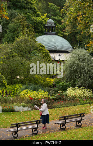 Valley Gardens, Harrogate, Yorkshire, England - lady walking on a path through this beautiful park, domed roof of café, shrubs and trees beyond. Stock Photo