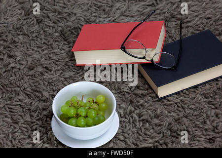 Two reading books laying on a shaggy grey rug with glasses and a bowl of grapes Stock Photo