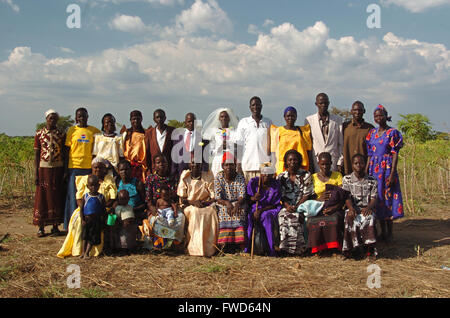 Lacekocot, Pader, Uganda. Friends and family gather for the traditional wedding photograph at the wedding of Acholi couples on a refugee camp in Africa. The bride and groom are wearing traditional western dress, donated by charities in the UK. The bride is wearing a white wedding dress. The guests are in brightly coloured traditional African dress,