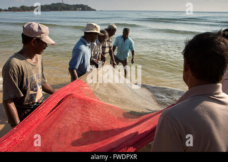 Sri Lanka, Trincomalee, Dutch Bay, fishermen fishing hauling in red horseshoe net from shore Stock Photo