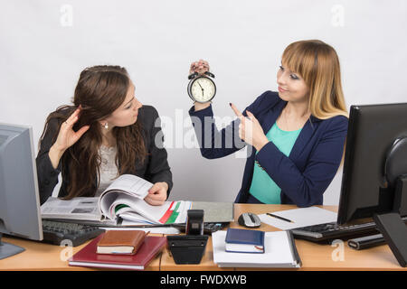 Girl shows a colleague in the office the rest of the working time on the clock Stock Photo