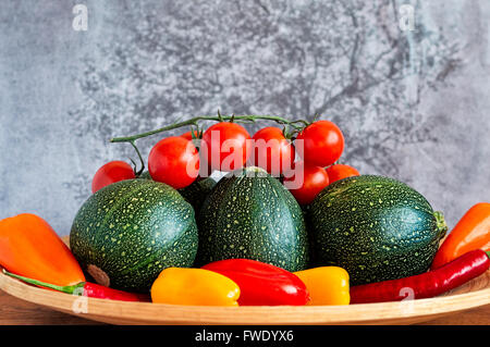 Selection of eight ball zucchini, cherry tomatoes, chili peppers and yellow, orange and red peppers on a bamboo plate. Stock Photo