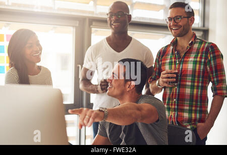 Handsome young adult showing something on his computer to a group of three male and female casually dressed friends holding drin Stock Photo