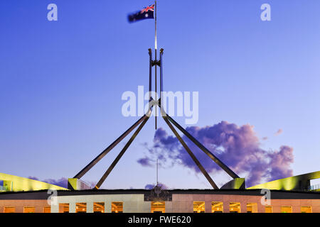 roof top part of Canberra parliament house - flagpole on four legs with flag and coat of arms at susnet with illumination. Stock Photo