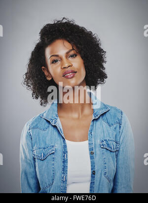 Portrait of tranquil woman in blue jean shirt and white top smiling sweetly against a gray background Stock Photo