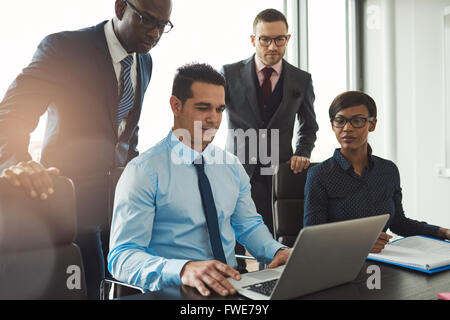 Group of diverse business people in formal clothing inside their office discussing or looking at information on a laptop compute Stock Photo