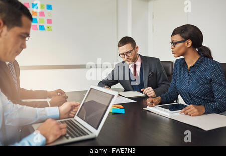 Group of multiracial business colleagues in a meeting seated around a table in the office working on laptops and paperwork Stock Photo