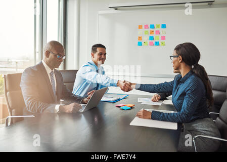 Two business colleagues shaking hands across the table in congratulations during a multiracial business meeting at a conference Stock Photo