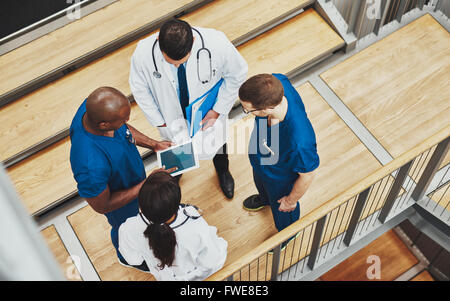 Multiracial medical team having a discussion as they stand grouped together around a tablet computer on a stair well, overhead v Stock Photo