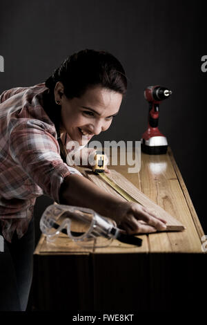 Young adult Hispanic woman measuring a wooden board with a tape measure Stock Photo