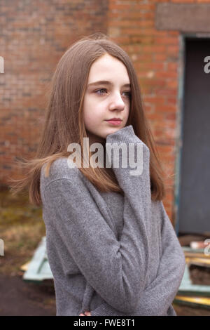 Pretty young teenage girl huddling in her jumper with a derelict building in the background Stock Photo