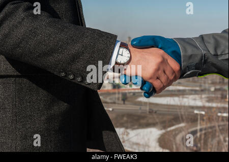 Industry worker with glove shakes hands with businessman Stock Photo