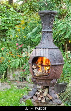 Rustic cast iron wood burning stove, Mexican chiminea, with flames, ready for barbecue, in summer cottage flower garden Stock Photo