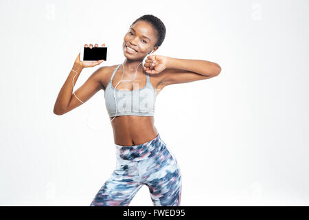 Happy pretty young african american sportswoman listening to music from blank screen smartphone and dancing over white backgroun