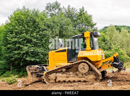 Yellow and black small bulldozer covered in mud. Stock Photo