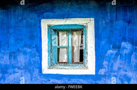 Old window with cyan wooden frame  and crocheted curtain on a blue plastered hand painted wall. Stock Photo